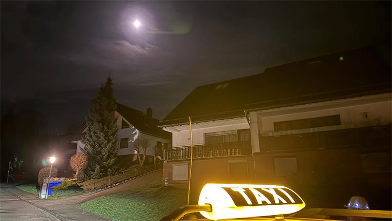 Ein Taxi steht nachts vor einem Haus.