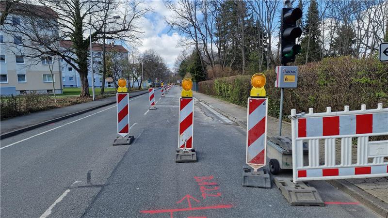 Straße mit mehreren rot-weißen Absperrpfosten und einer rot-weißen Absperrung neben einer Ampel und einem Warnschild.