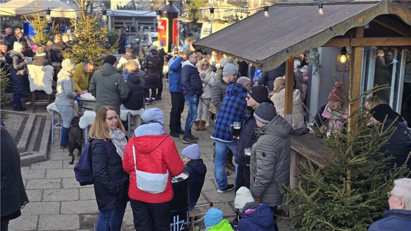 Menschenmenge vor einem Holzstand auf einem Weihnachtsmarkt bei Tageslicht.