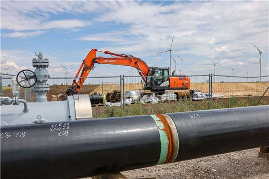 Die Rohre einer künftigen Wasserstoffleitung liegen vor der Kulisse eines Windparks.
