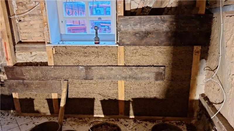 Innenwand mit Dämmmaterial und Holzlatten unter einem Fenster in einem Raum im Rohbau.