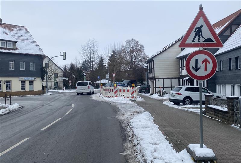 Straße in einem verschneiten Ort mit Baustellenschild und Verkehrszeichen für einspurig wechselnden Verkehr.
