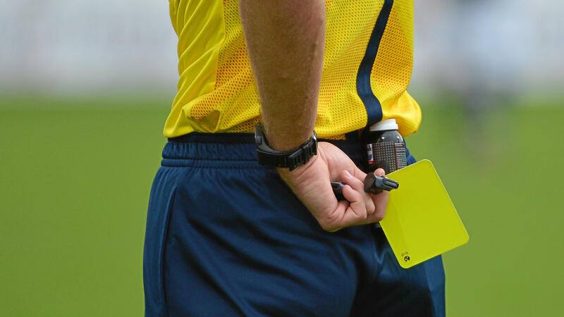 Schiedsrichter hält gelbe Karte hinter dem Rücken auf einem Fußballfeld