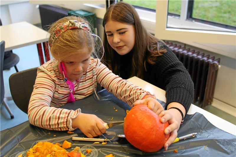 Die Schüler helfen den Kindern beim Kürbisschnitzen. Foto: Jenzora