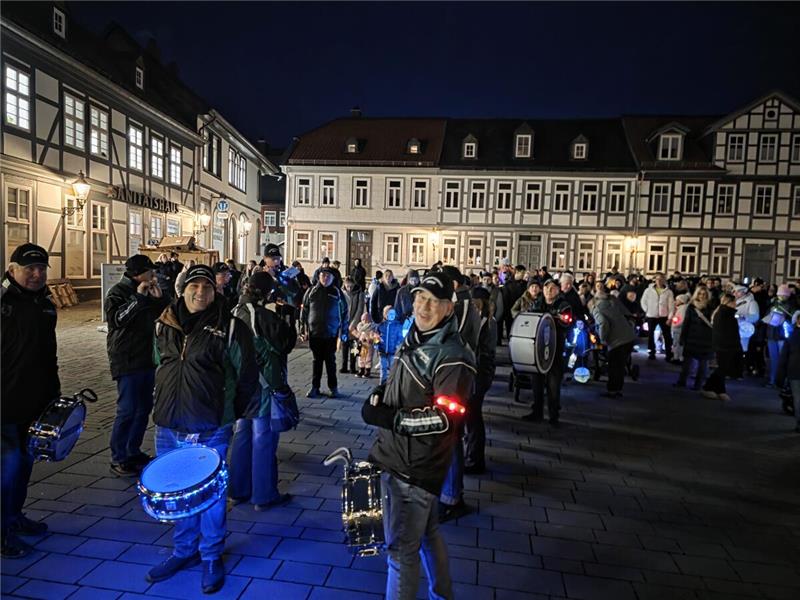 Menschen mit Instrumenten stehen auf einem großen Platz in der Innenstadt im Dunkeln.