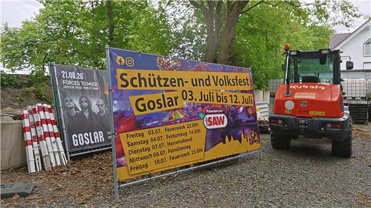 Werbebanner für das Schützen- und Volksfest Goslar vom 3. bis 12. Juli neben einem roten Kubota-Bagger auf einem Schotterweg.
