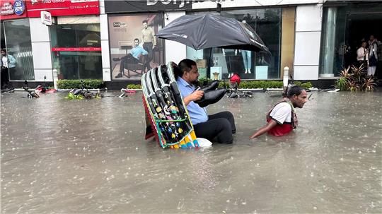 Die Schuhe bleiben trocken: Ein Mann lässt sich in Bangladesch in einer Rikscha durch eine überflutete Straße fahren. 