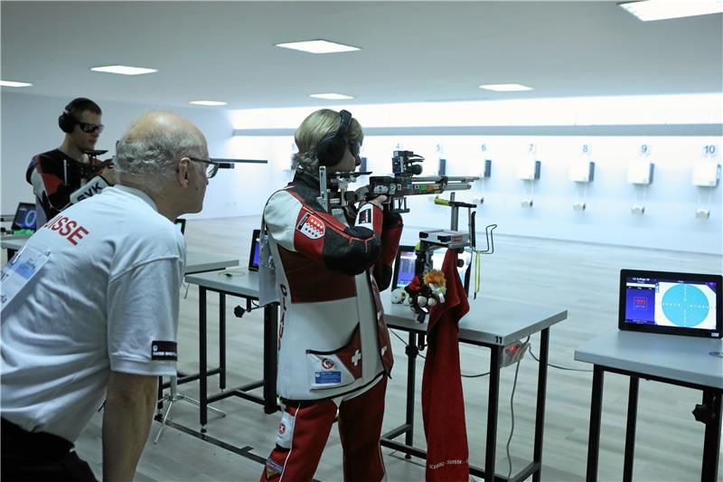 Adamek gewinnt das Stehendschießen Die Schweizerin Claudia Kunz-Inderkummen mit ihrem Betreuer während des Qualifikationsschießens. Im Hintergrund nimmt der spätere Sieger, Martin Adamek aus Tschechien, sein Luftgewehr in die Hand. Foto: Neuendorf