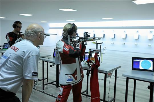 Die Schweizerin Claudia Kunz-Inderkummen mit ihrem Betreuer während des Qualifikationsschießens. Im Hintergrund nimmt der spätere Sieger, Martin Adamek aus Tschechien, sein Luftgewehr in die Hand.  Foto: Neuendorf