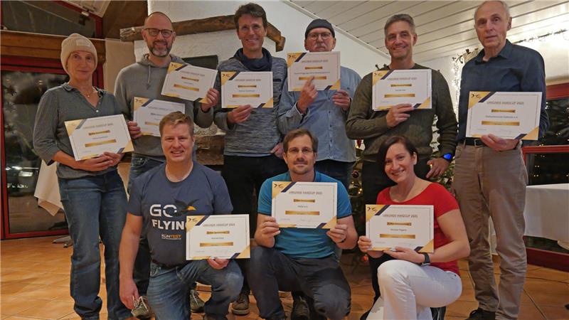 Gruppe von neun Personen in einem Raum, die jeweils eine Urkunde in den Händen halten, einige stehen, andere knien.