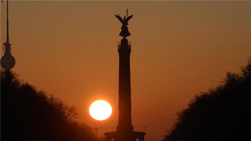 Die Sonne geht am Morgen bei wolkenlosem Himmel hinter der Siegessäule in Berlin auf.