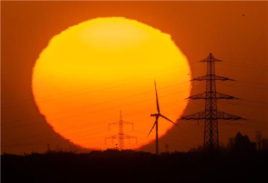 Die Sonne geht hinter Windrädern und Hochspannungsleitungen in der Region Hannover auf.