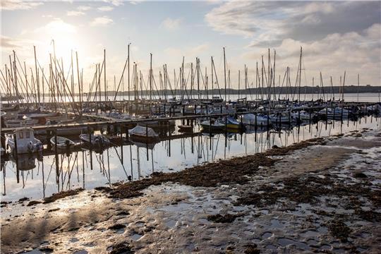 Die Sonne scheint auf einen Bootshafen an der Kieler Förde, aus dem das Sturmtief «Poly» das Wasser herausgedrückt hat, so dass die normalerweise mit Wasser bedeckten Ufer trocken liegen.