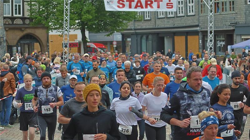 Läufergruppe startet bei einem Stadtlauf unter einem Banner mit der Aufschrift START auf einem gepflasterten Platz vor historischen Gebäuden.