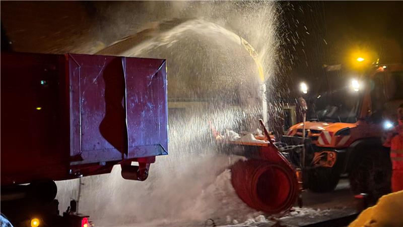 Das Foto zeigt eine Schneefräse, die Schnee auf die Ladefläche eines Lastwagens schleudert.