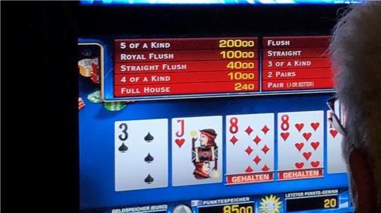 Das Bild zeigt eine Frau, die vor einem Geldspielautomaten sitzt.