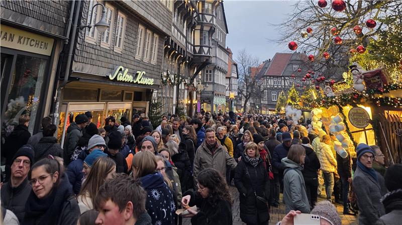 Menschenmenge auf einer belebten Straße mit Fachwerkhäusern und weihnachtlich geschmückten Ständen am späten Nachmittag.