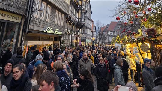 Menschenmenge auf einer belebten Straße mit Fachwerkhäusern und weihnachtlich geschmückten Ständen am späten Nachmittag.