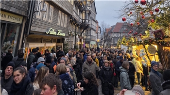 Menschenmenge auf einer belebten Straße mit Fachwerkhäusern und weihnachtlich geschmückten Ständen am späten Nachmittag.