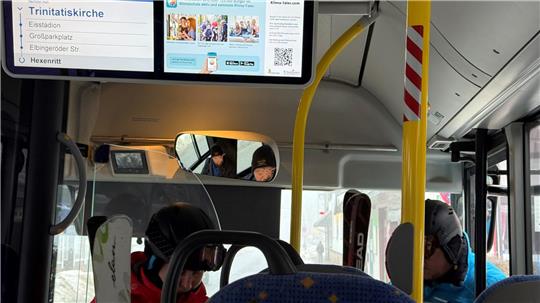 Das Foto zeigt zwei Wintersportler, die mit Skiern in einen Bus einsteigen.