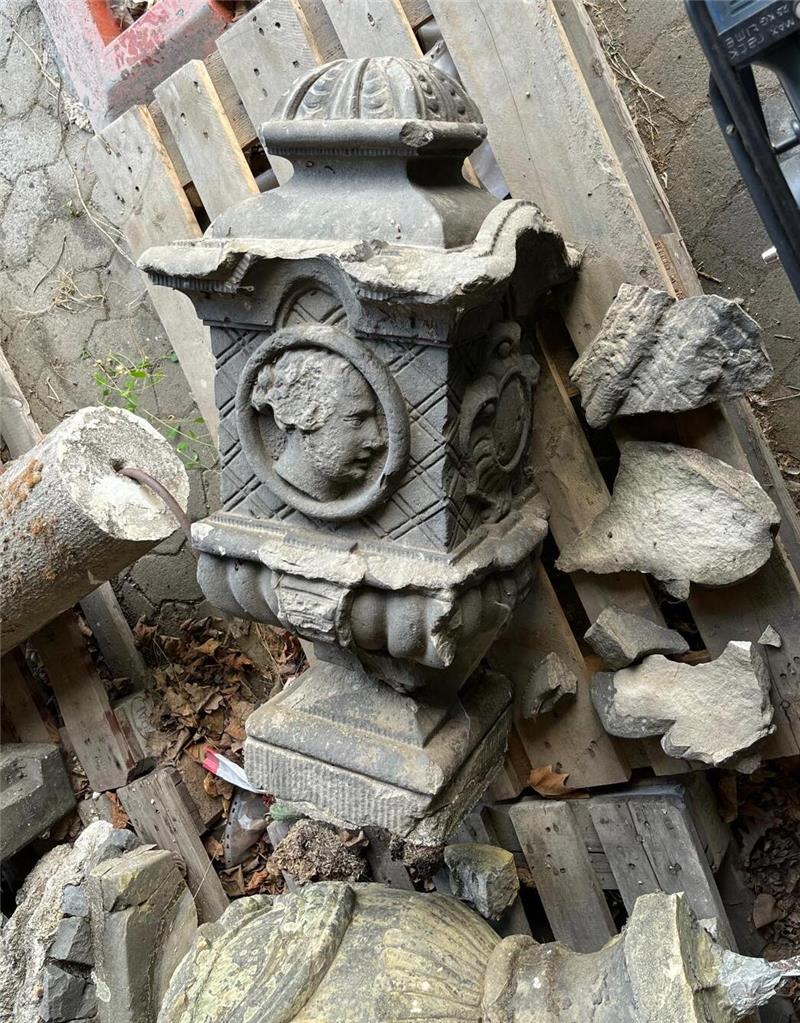 Historische Steinvase kehrt nach Jahren an Ursprungsort zurück Steinerne, verzierte Säulenteile und Bruchstücke liegen auf Holzpaletten auf einem gepflasterten Boden.