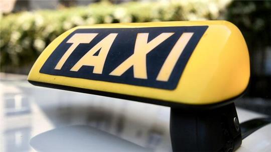 Gelbes Taxi-Dachzeichen mit schwarzer Schrift 'TAXI' auf einem Fahrzeugdach.