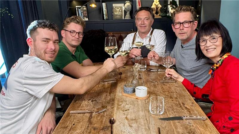 Fünf Menschen sitzen rund um einen Tisch und stoßen an.