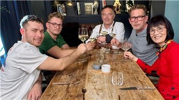 Fünf Menschen sitzen rund um einen Tisch und stoßen an.