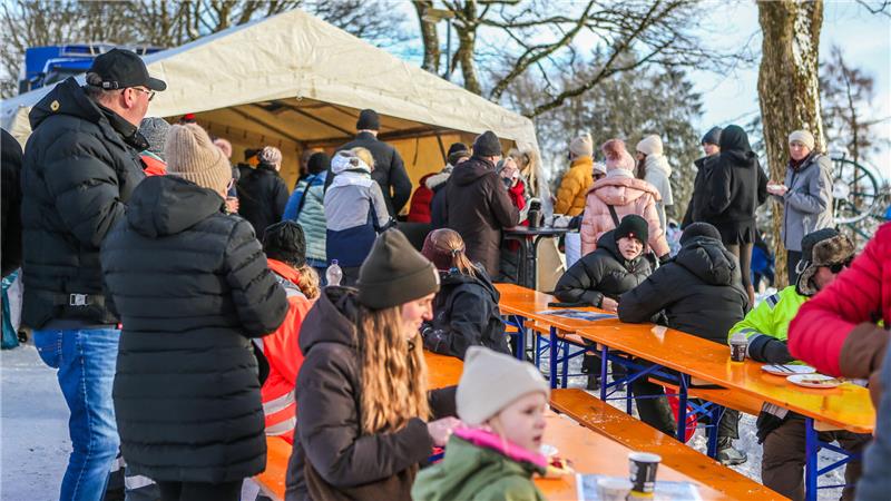 Das Foto zeigt Menschen, die warm angezogen vor einem Zelt auf Bänken an Tischen sitzen.