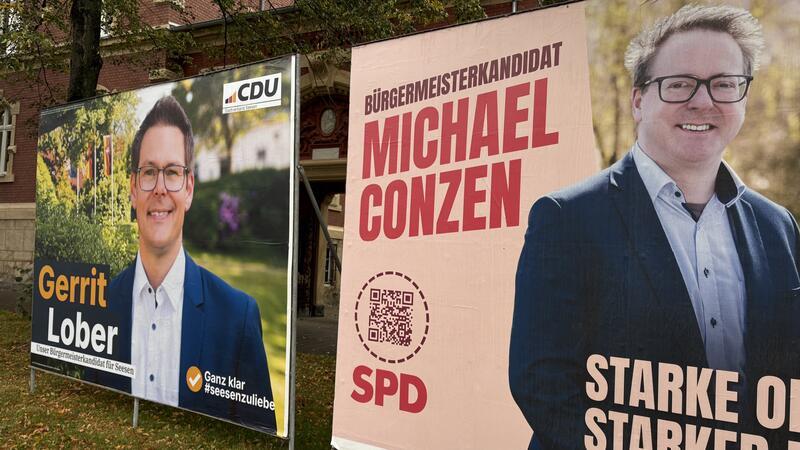 Zwei nebeneinander stehende Wahlplakate mit Porträtfotos von Männern in Anzügen, links mit dem Namen Gerrit Lober und CDU-Logo, rechts mit dem Namen Michael Conzen, SPD-Logo und dem Text 'Bürgermeisterkandidat'.