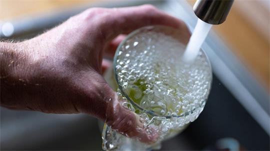 Hand hält ein Glas unter fließendem Wasserhahn mit schäumendem Wasser