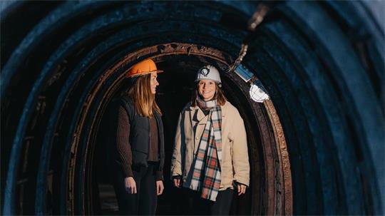Zwei Frauen mit Schutzhelmen stehen in einem dunklen Tunnel und schauen sich an.