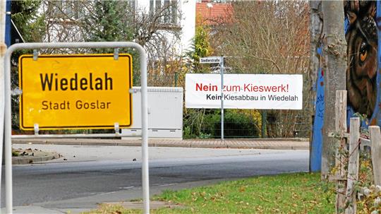 Hinter dem Ortsteingangsschild Wiedelah hängt ein Plakat am Zaun: Nein zum Kieswerk!