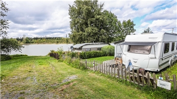 Der Campingplatz Prahljust liegt idyllisch am Pixhaier Teich. Im Vordergrund ist ein Wohnwagen zu sehen.