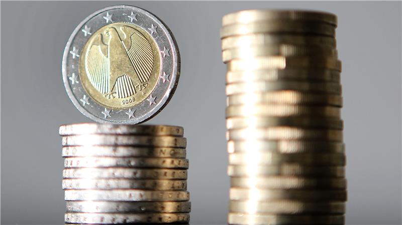 Ein Stapel Euro-Münzen mit einer einzelnen Münze, die auf der Kante steht, im Vordergrund und einem unscharfen Münzstapel im Hintergrund