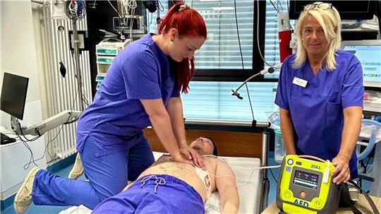 Die beiden Fachschwestern Linda Baumgarten (li.) und Marion Kruse demonstrieren an einem Kollegen eine simulierte Reanimation mit einem Defibrillator.