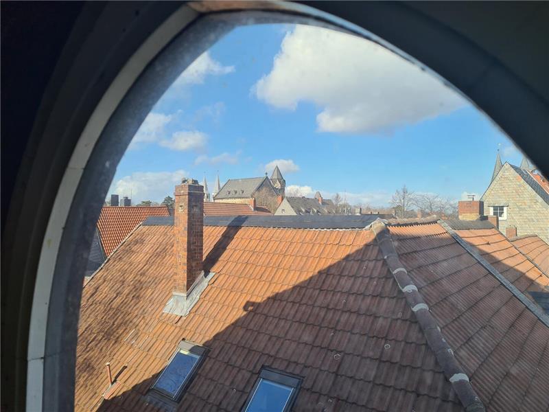 Blick durch ein ovales Fenster über die Dächer in den blauen Himmel. 