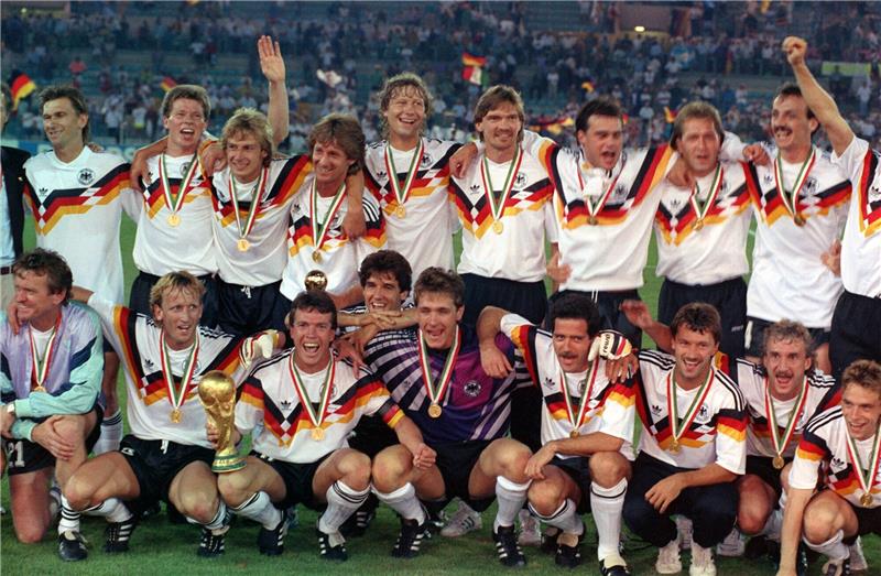 Zum Tod von Andy Brehme: Sein Leben in Bildern Die deutsche Mannschaft stellt sich nach dem 1:0-Finalsieg gegen Argentinien bei der Fußball-Weltmeisterschaft am 08.07.1990 im Olympiastadion von Rom zum Mannschaftsfoto auf: Stehend (v.l.): Klaus Augenthaler, Stefan Reuter, Jürgen Klinsmann, Frank Mill, Guido Buchwald, Paul Steiner, Thomas Berthold, Andreas Köpke, Jürgen Kohler; Hockend (v.l.): Torwart-Trainer Sepp Maier, Andreas Brehme, Lothar Matthäus (mit dem WM-Pokal), Karlheinz Riedle, Bodo Illgner, Uwe Bein, Günter Hermann, Rudi Völler, Thomas Häßler. Foto: Frank Leonhardt/dpa