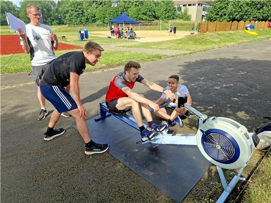 Die drei Physiker geben auf der Rudermaschine alles, sie wollen die Sommerspiele gewinnen. Im Hintergrund steht Dr. Sebastian Sdrenka, der künftig das Sportinstitut leitet. Foto: Knoke