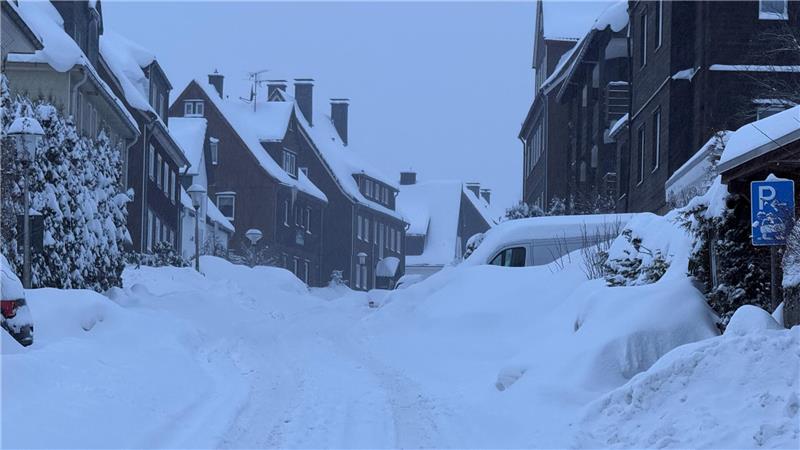 Da Foto zeigt eine verschneite Straße mit Schneebergen an den Seiten.