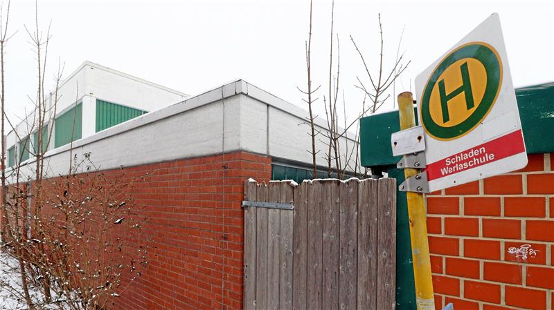Ein Bushaltestellenschild steht vor einer mit Klinkersteinen errichteten Halle.