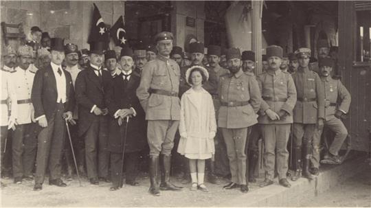 Gruppenaufnahme von Männern in Militär- und Ziviluniformen sowie ein Mädchen in hellem Kleid vor einem Gebäude mit Säulen