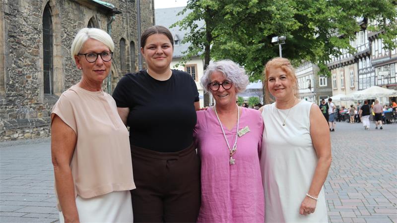 Vier Frauen stehen nebeneinander auf einem gepflasterten Platz vor einem historischen Gebäude und lächeln in die Kamera.