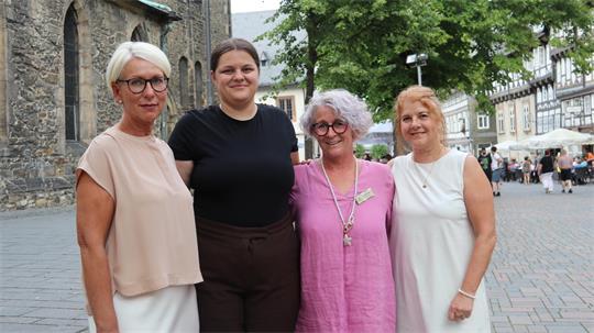 Vier Frauen stehen nebeneinander auf einem gepflasterten Platz vor einem historischen Gebäude und lächeln in die Kamera.