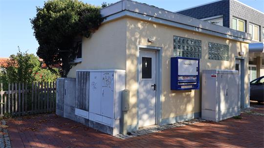 Kleines Gebäude mit weißer Tür, blauer Briefkasten und mehreren weißen Schaltkästen davor