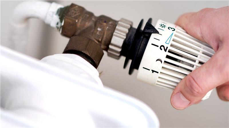 Eine Person dreht am Thermostat eines Heizkörpers. 