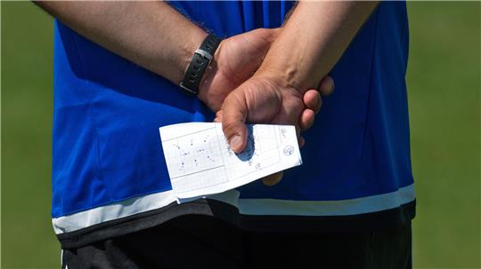 Person in blauem T-Shirt hält hinter dem Rücken ein Blatt Papier mit Skizzen und Notizen