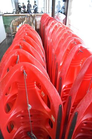 Mehrere rote Kunststoffschlitten sind eng in zwei Reihen hintereinander aufgestellt und mit Draht verbunden.