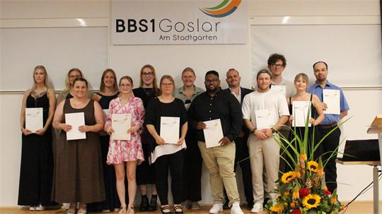 Mit einer Urkunde in den Händen stehen 14 Frauen und Männer nebeneinander.