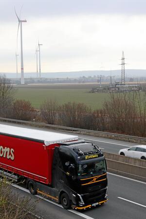 Eine Autobahn mit Windrädern und einem Umspannwerk im Hintergrund.